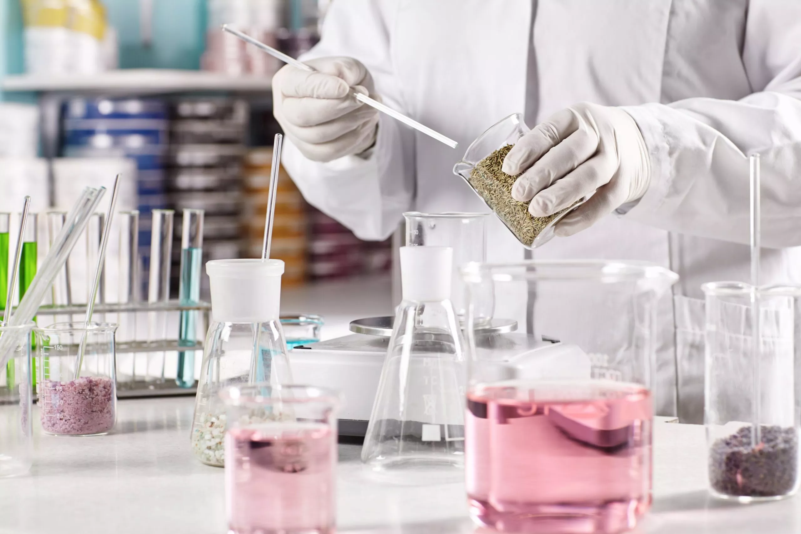 Biotechnology and pharmacology concept. Laboratory young clever worker standing near table surrounded with glass beakers filled with colorful liquid working at discovering new kind of vegetation.